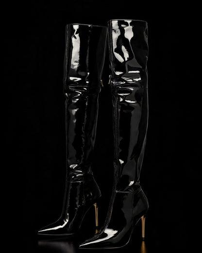 Bota vinil preta over the knee com bico fino e salto agulha dourado, sobre fundo preto