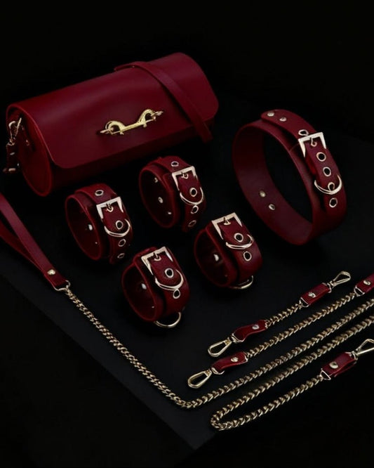 Kit BDSM Luxury em couro sintético vinho com algemas, coleira, correntes e bolsa, sobre fundo preto
